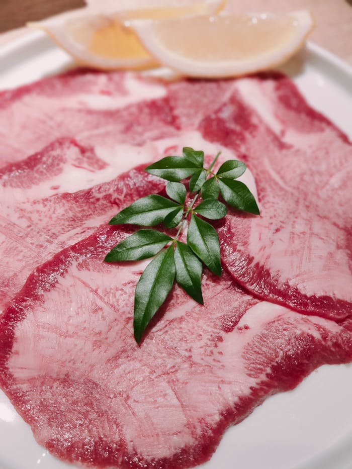 Close-up of raw beef slices garnished with lemon and fresh herbs on a plate.